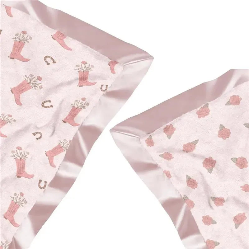 Reversible baby blanket featuring pink boots with flowers and a floral pattern, edged with satin trim.