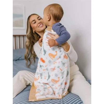 Reversible baby blanket by Jujube featuring playful dinosaur designs, being held by a smiling mother with her baby.