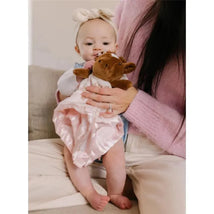 Baby holding a Jujube Security Blanket with a brown boot-themed plush toy while being cuddled by an adult.