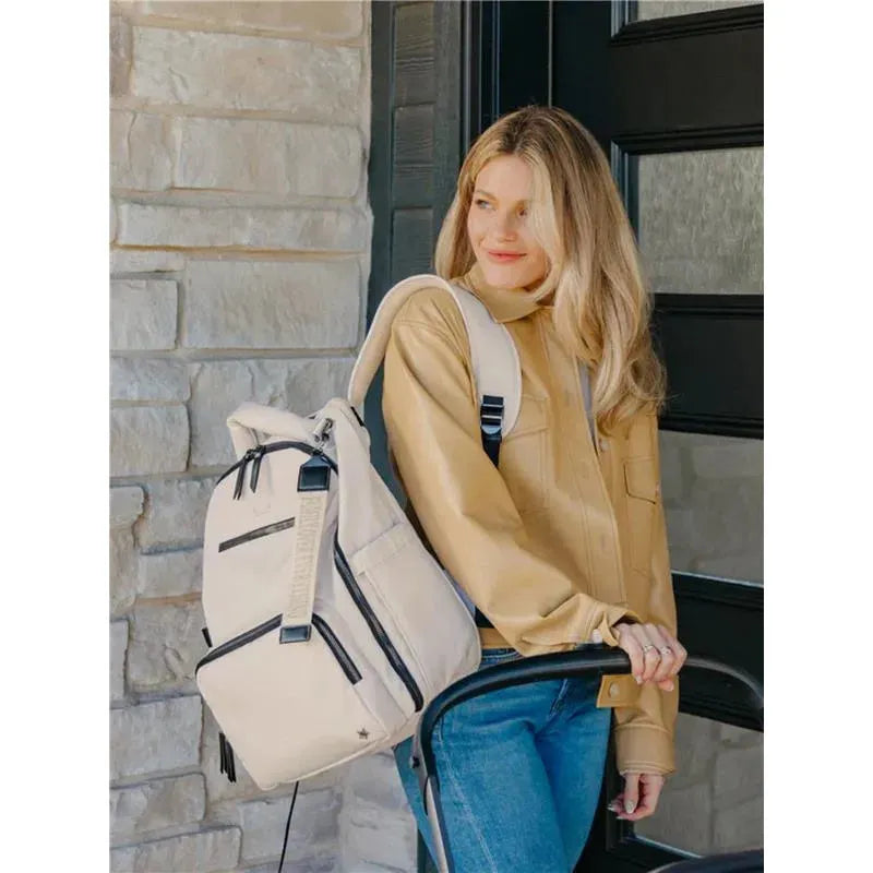 Classic Backpack in Cloud color, worn by a woman in a tan jacket, standing by a door with a stroller.