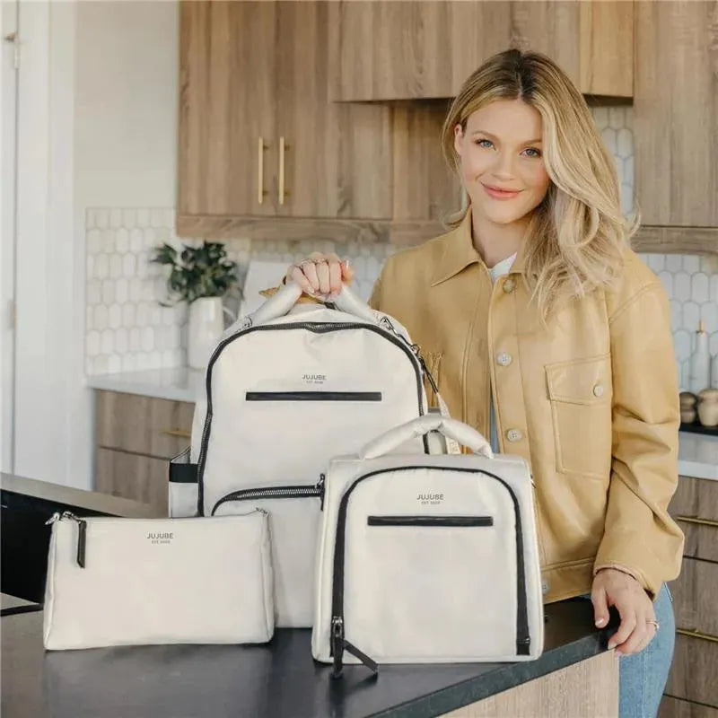 Insulated bottle bag and two other bags from Jujube x Witney Carson, displayed by a smiling woman in a kitchen setting.