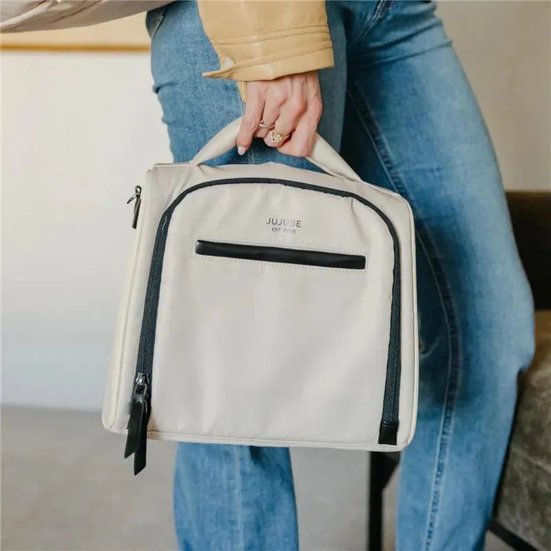 Insulated bottle bag by Jujube in Cloud color, featuring a front pocket and a top handle, held by a person.