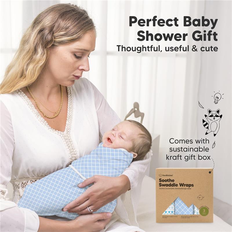 Mother holding a peacefully sleeping baby wrapped in a blue grid-pattern swaddle, with a kraft gift box nearby.