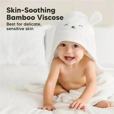 Smiling baby wearing a white hooded towel with lamb features, sitting on a soft blanket.