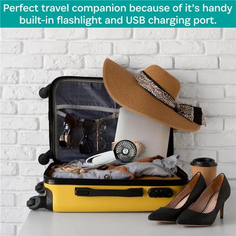 Yellow suitcase packed with clothing, a sunhat, sunglasses, a fan, a laptop, and a coffee cup against a white brick wall.