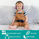 Toddler wearing pink Kidco Whispears headphones, seated on a light gray sofa, showcasing noise reduction features.