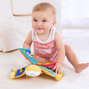 Smiling baby sitting on a carpet, engaging with a colorful, fabric crinkle book featuring farm animals.