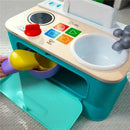 Colorful pretend kitchen toy with stove, control buttons, and a sink; includes a hand placing a yellow item into a purple bowl.