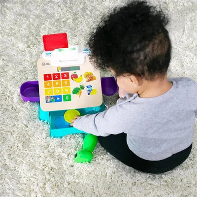 Child engaging with the Kids II Be + Hape Magic Touch Shopping Basket toy, featuring colorful buttons and food items.