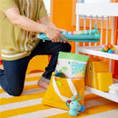 A person kneels while holding the folding toy bar of the Kids II Bright Starts Wild Wiggles Activity Gym, with colorful toy accessories nearby.