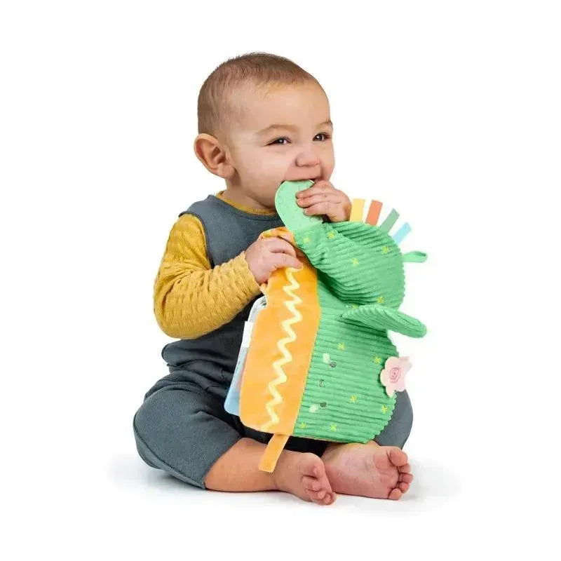Toddler sitting and biting on a soft, colorful teething activity book shaped like a dinosaur.