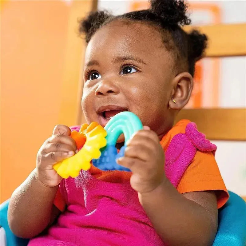 Infant happily holding colorful silicone teethers, with a joyful expression, seated in a chair.