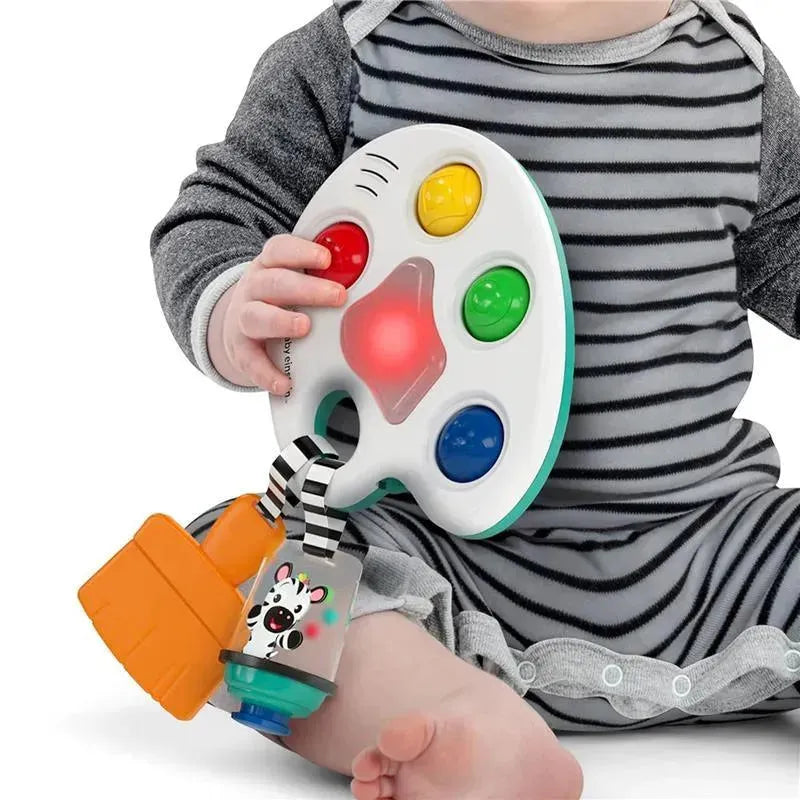 Sensory toy featuring a colorful palette with buttons and lights, held by a child sitting on a floor.