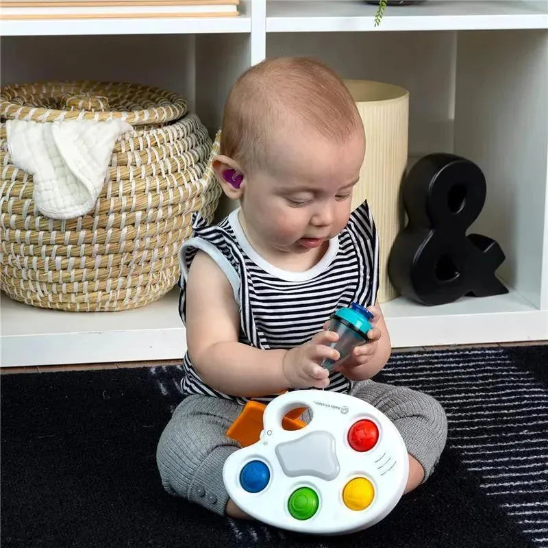 Infant playing with the Kids II Color Palette Popper Sensory Toy, exploring a blue container while seated on a rug.