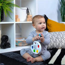 A baby in gray clothing sits on a black and white rug, holding a colorful Kids II Color Palette Popper sensory toy.