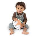 Smiling toddler sitting on the floor, holding a soft Kitt the Fox crinkle toy with colorful tags.