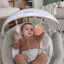 Baby in a brown outfit plays with a plush carrot toy in the Ingenuity InLighten Baby Bouncer Seat.