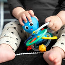 Bright blue octopus teether toy with colorful rings; a child is holding it while sitting on a patterned mat.