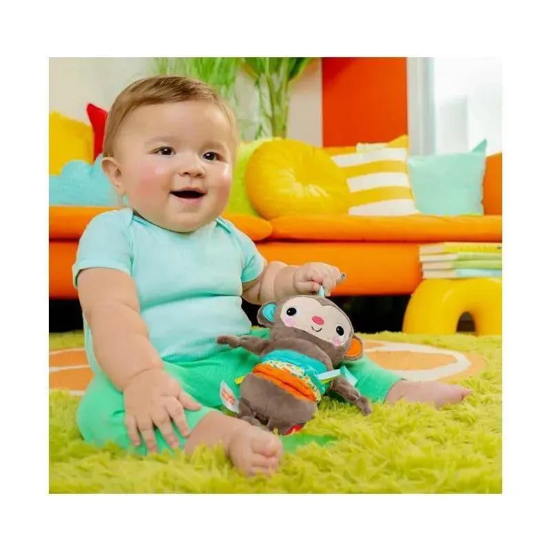 Smiling baby in turquoise outfit sits on a bright green rug, holding a Pull, Play ’N Boogie Monkey toy.