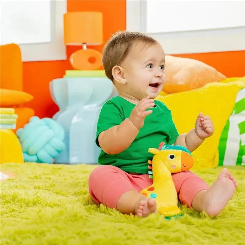 Baby sitting on a colorful rug, happily engaged with a yellow giraffe rattle and teether toy.