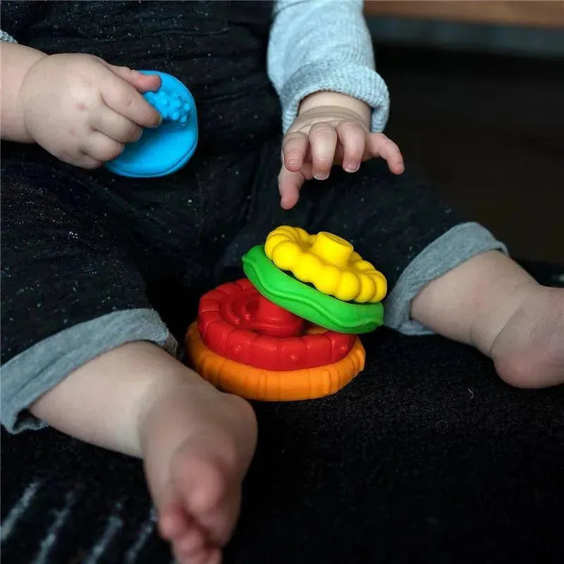 Multi-textured teether toy featuring colorful stacking rings, held by a child sitting on a black surface.
