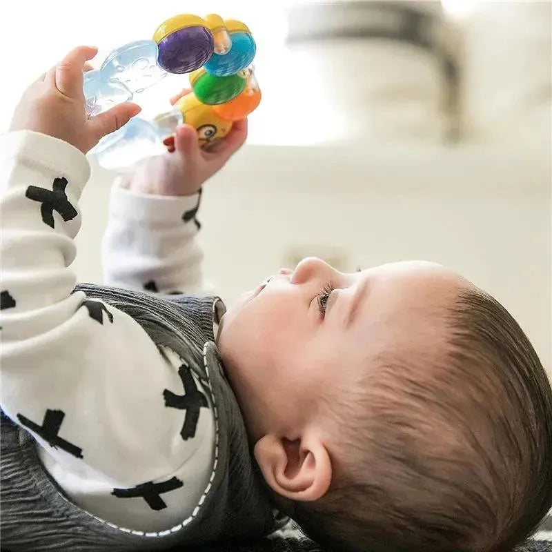 Baby playing with a colorful Kids II Teether-Pillar Rattle Toy, engaging with the toy while lying down.