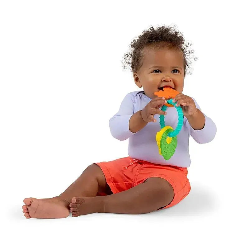 Toddler sitting on the floor, holding the Kids II Tropical Chews teething ring, featuring colorful leaf and fruit shapes.