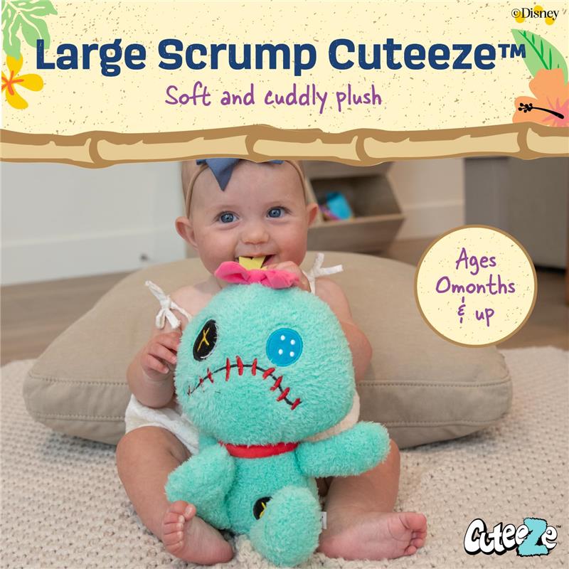 A baby smiles while holding a soft, plush Scrump doll, featuring a teal color, stitched face, and a bow.