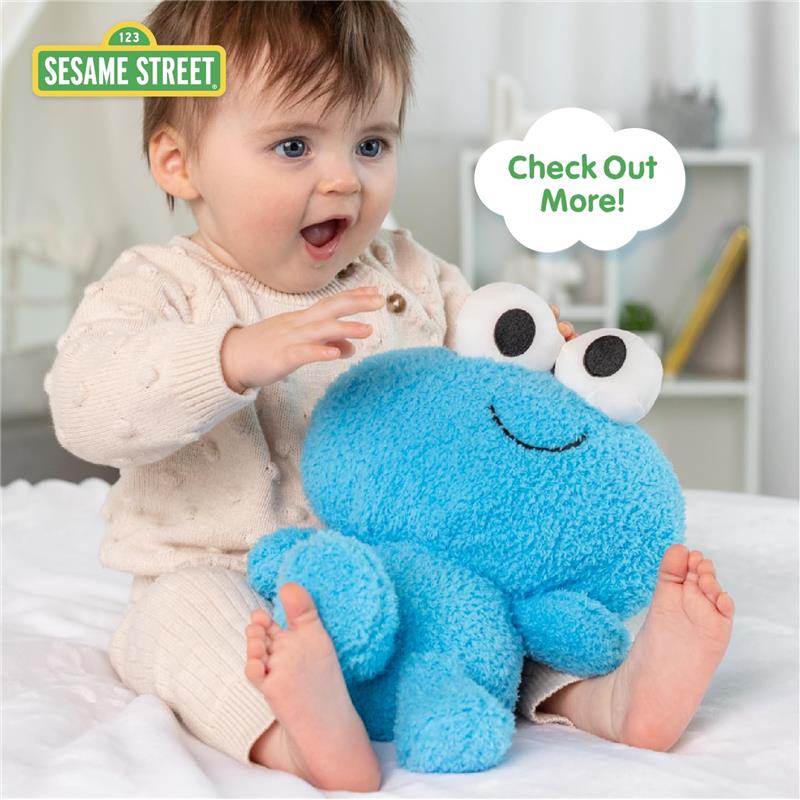 Baby joyfully plays with a blue Sesame Street Elmo plush toy, featuring large eyes and a smile, on a soft surface.