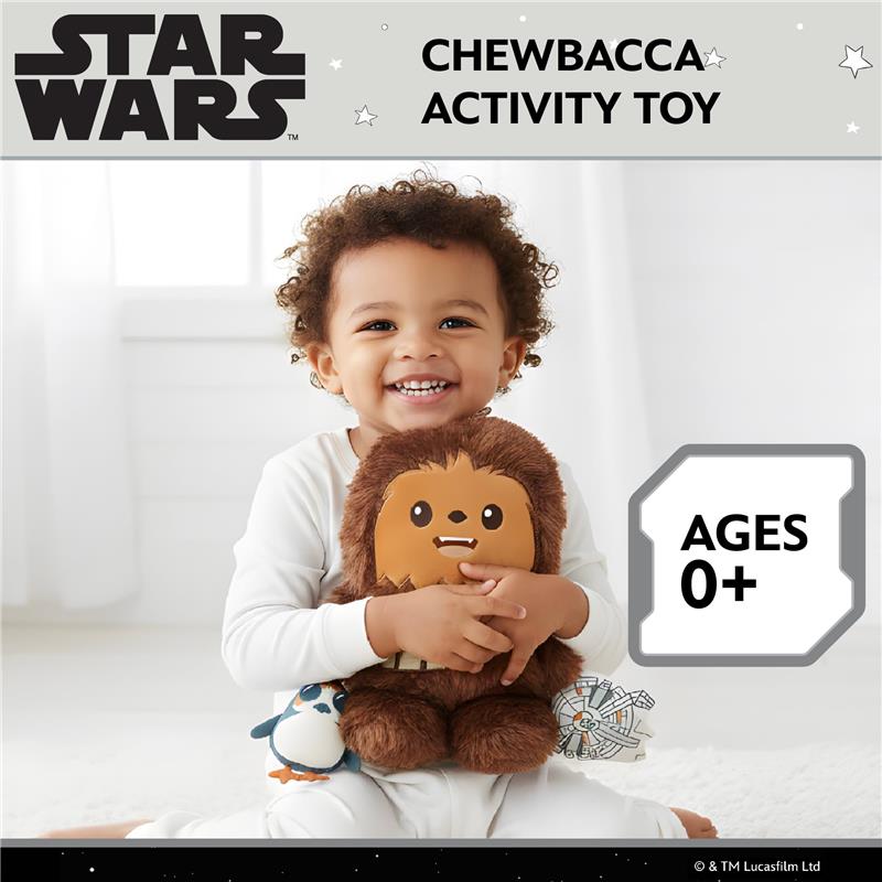 A smiling child holds a plush Chewbacca activity toy while wearing a white outfit. Ages 0+ indicated.