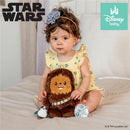 Child sitting on a bed, holding a plush Chewbacca toy wearing a bandolier, with a penguin toy nearby.