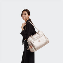 Kipling Alanna Baby Bag in Quartz Metallic being carried by a woman, featuring a zippered front pocket and floral keychain.