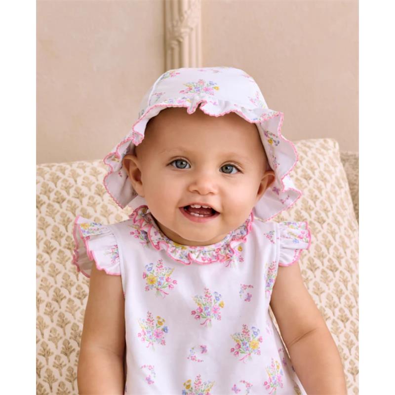 Smiling baby wearing a Kissy Kissy Pastel Gardens floppy hat with floral patterns, sitting on a patterned sofa.