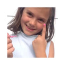 Girl with a pink nail polish on her finger, smiling and pointing to her decorated nail, holding a small brush.