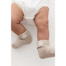 Baby legs wearing Kyte Baby neutral socks in cloud, oat, and sage colors, featuring a simple design with light accents.