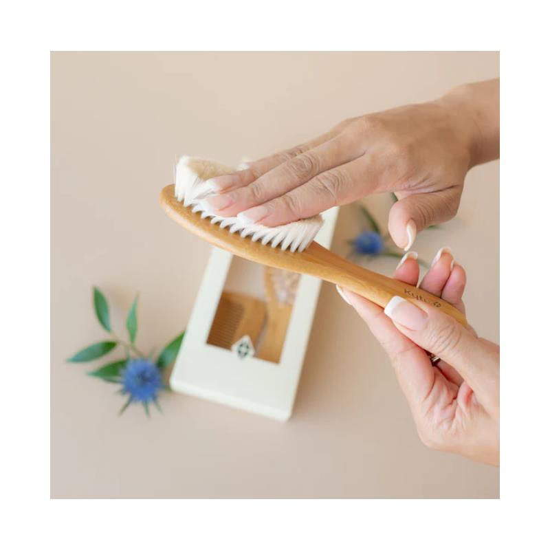 Kyte Baby 3-pack brush set featuring a bamboo brush, with a hand using it gently on a surface.