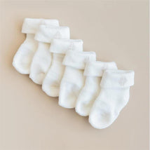 Three pairs of white infant socks with folded cuffs arranged neatly on a neutral background.