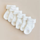 Three pairs of white infant socks with folded cuffs arranged neatly on a neutral background.