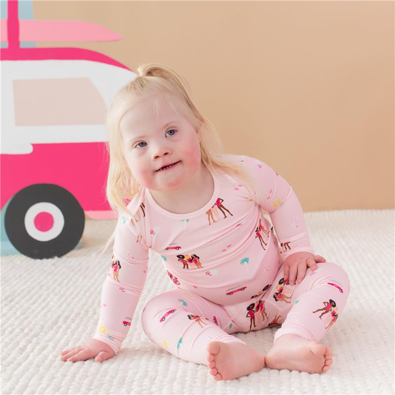 Baby girl wearing pink long sleeve pajamas featuring Barbie™ beach-themed prints, sitting on a textured blanket.