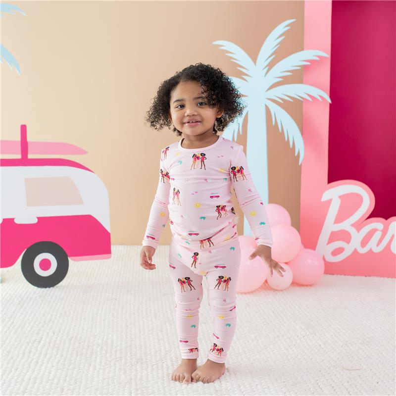 Baby girl wearing long sleeve pink pajamas with Barbie™ beach graphics, standing on a textured floor.