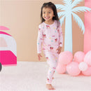 Baby girl wearing long sleeve pink pajamas with Barbie™ beach print, smiling while standing on a soft rug.