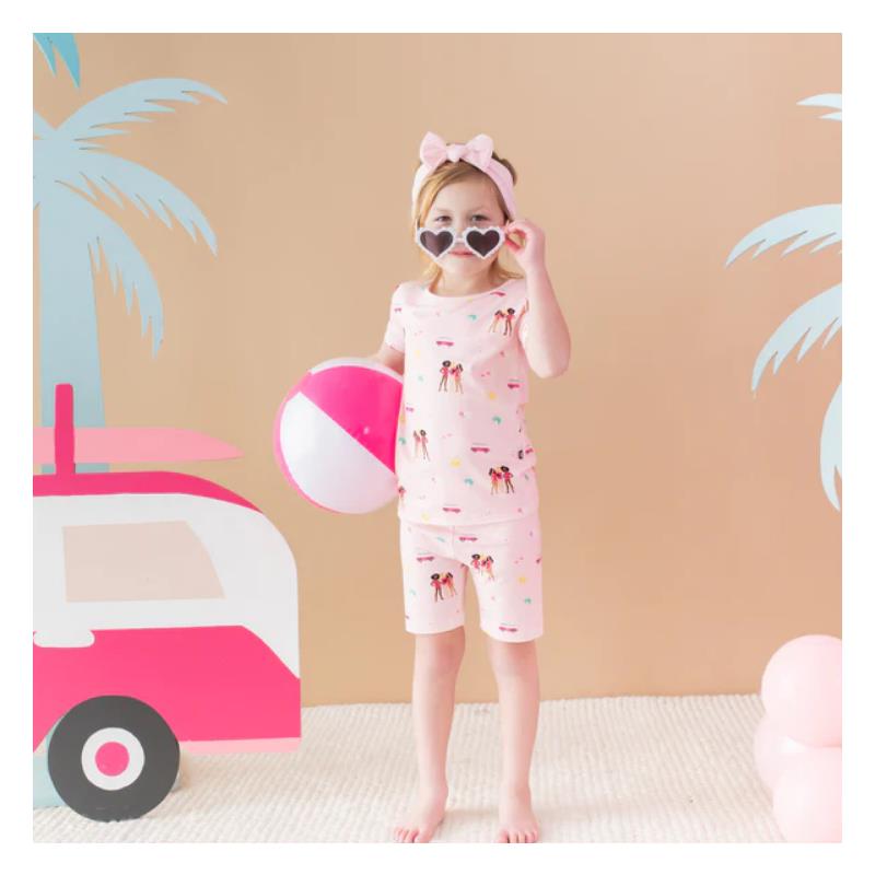 Baby girl in pink short sleeve pajamas with Barbie™ beach theme, holding a beach ball and wearing heart-shaped sunglasses.