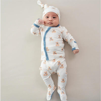 Baby girl in a teddy bear-print outfit with blue accents and matching cap, lying on a light background.