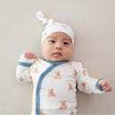 Baby girl wearing a teddy bear-print bodysuit with a matching cap, lying down on a light background.