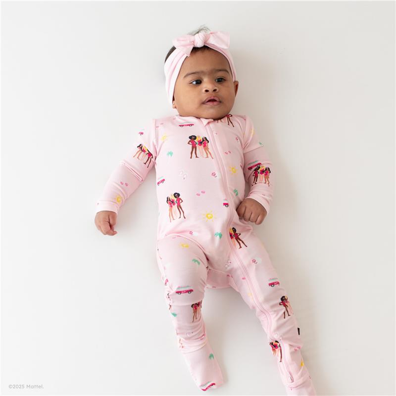 Baby girl in a pink zippered footie adorned with Barbie™ beach graphics and a matching headband, lying on a white surface.
