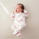 Baby girl wearing a white zippered footie with pink bow print, lying on a soft surface and yawning.