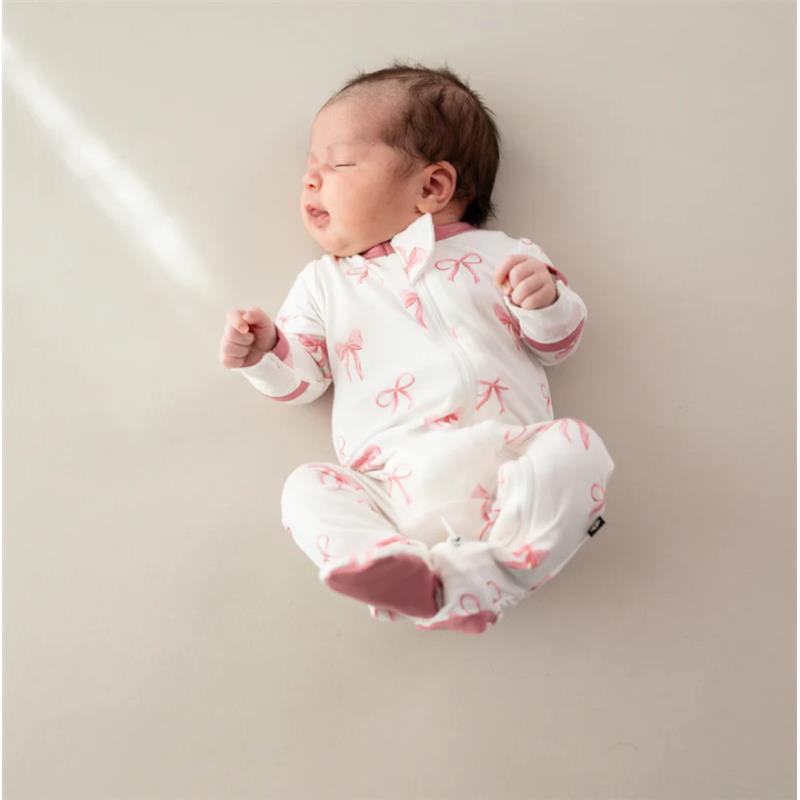 Baby girl in a white zippered footie featuring pink bows, resting on a light background with a peaceful expression.