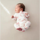 Baby girl in a white zippered footie featuring pink bows, resting on a light background with a peaceful expression.