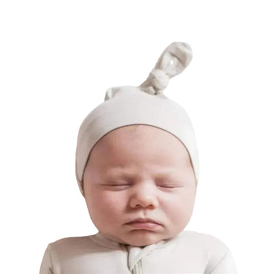 Bamboo baby knotted cap in oat worn by a sleeping baby, featuring a soft, neutral color and a tied knot on top.