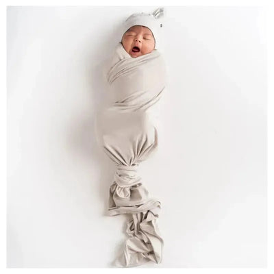 Bamboo baby knotted cap and swaddle in oat color, featuring a sleeping infant wrapped snugly.